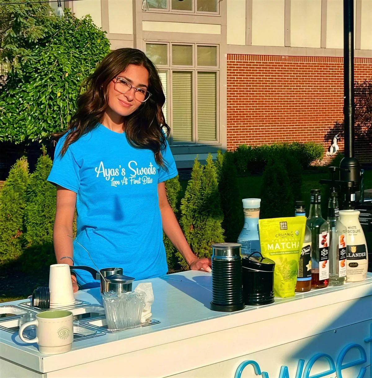 Aya Islim at her matcha and coffee cart, wearing an Aya's Sweets shirt